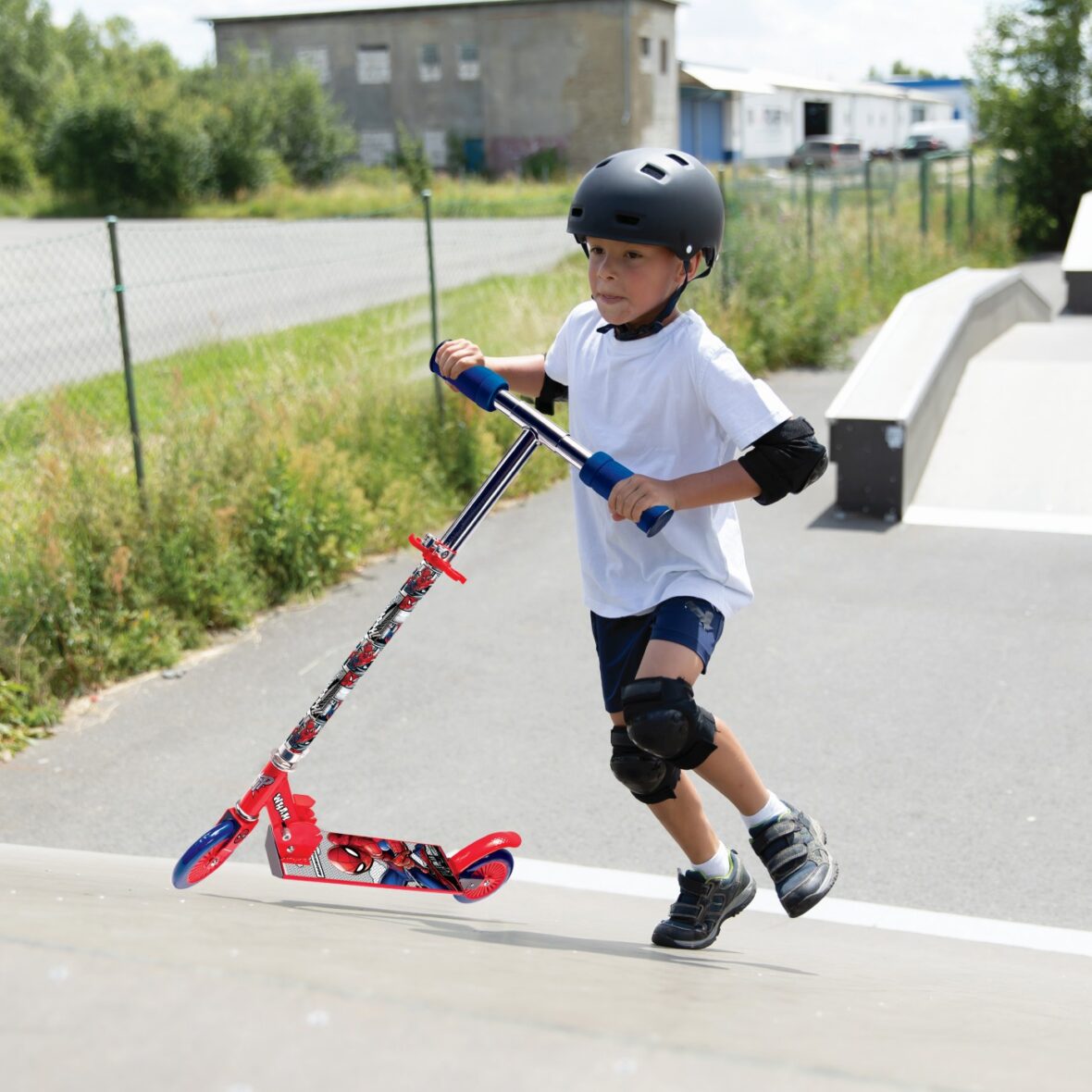 A cute little boy rides a scooter in a skatepark.