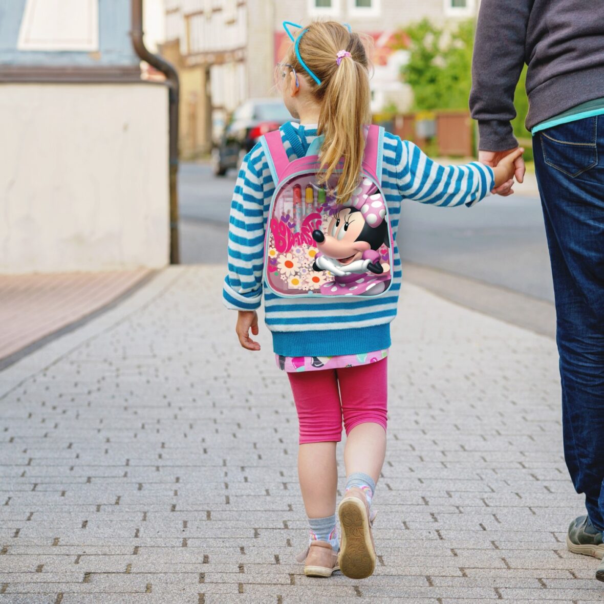 Happy child preschool girl smiles and holds father’s hand on the way to school on the first sunny day of class. Dad and daughter on the way to kindergarten, fun together. Child with glasses.