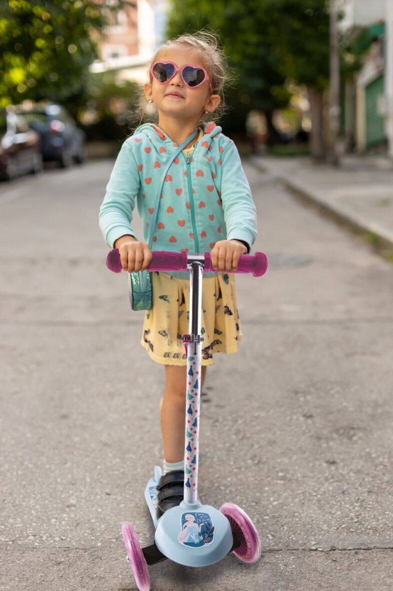 Happy little girl with sunglasses, playing with his scooter outd